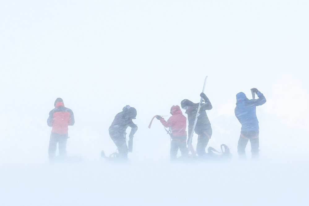 Inspiring explorers fighting to manage their climbing skins while taking them off in the wind during their crossing of South Georgia