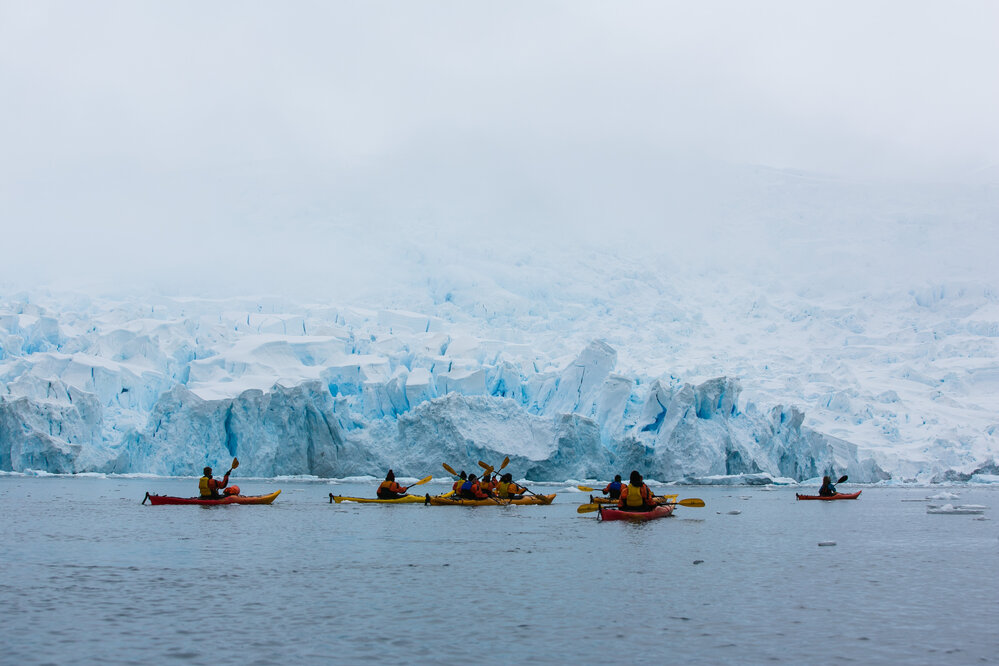 Inspiring Explorers kayak in front of Antarctic peninsula glacier