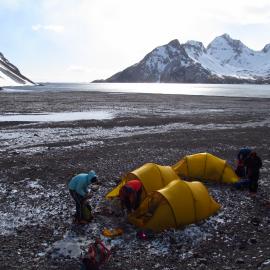 The team pitching three tents on Stoney ground with a bay and mountains in the background